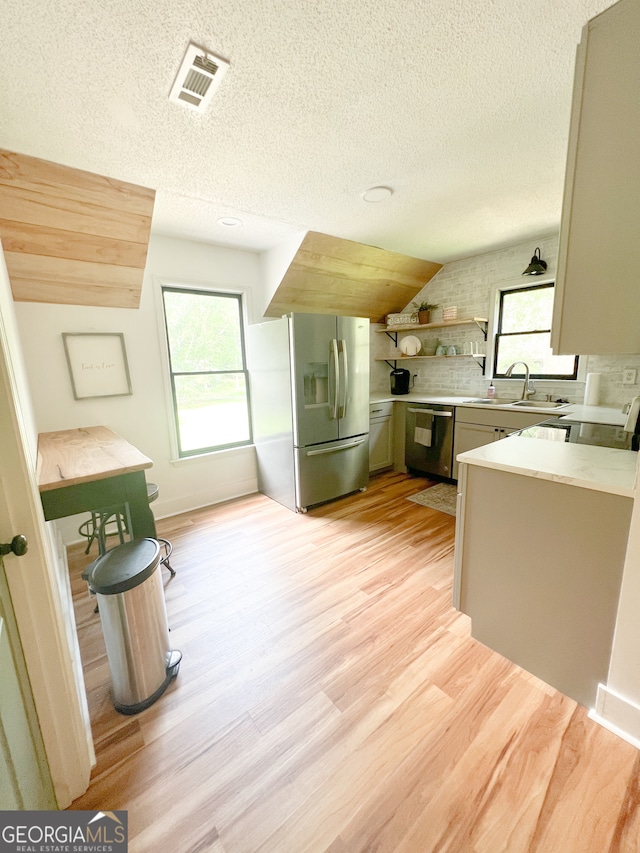 kitchen featuring sink, stainless steel appliances, backsplash, light hardwood / wood-style floors, and a textured ceiling