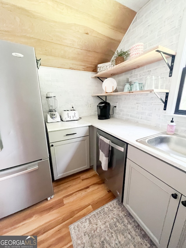 kitchen with tasteful backsplash, light hardwood / wood-style floors, stainless steel appliances, gray cabinets, and lofted ceiling