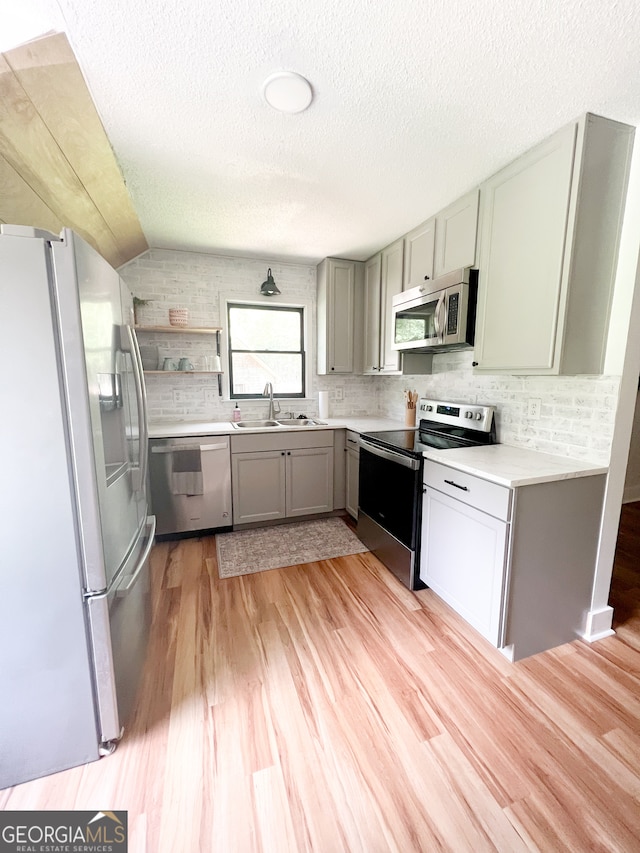 kitchen featuring sink, light wood-type flooring, vaulted ceiling, and appliances with stainless steel finishes