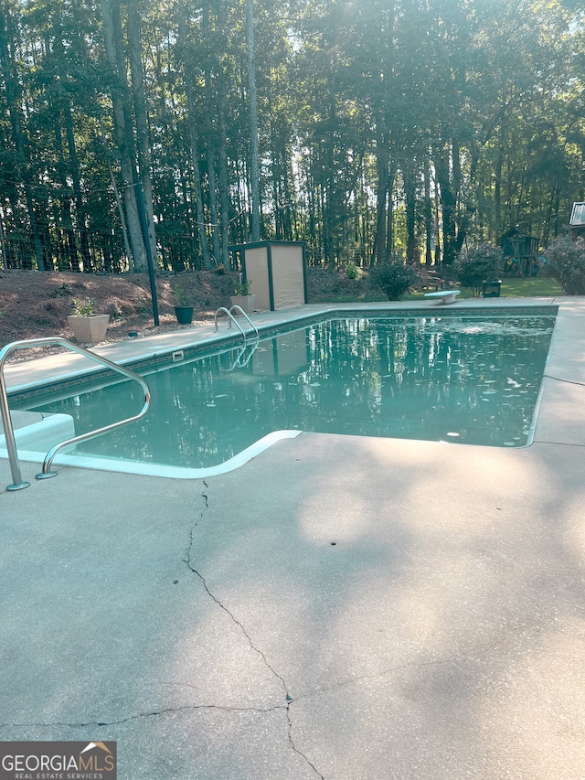 view of swimming pool with a storage unit and a diving board