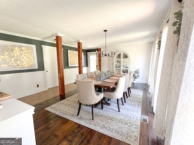 dining space with ornate columns, dark hardwood / wood-style floors, crown molding, a chandelier, and a textured ceiling