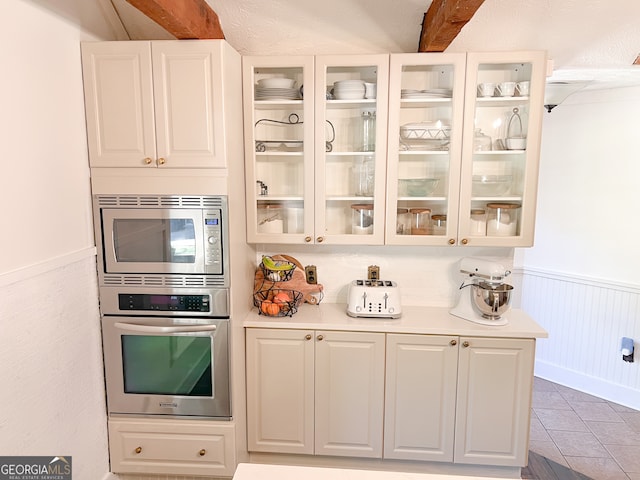 kitchen featuring white cabinetry, beamed ceiling, light tile patterned flooring, and appliances with stainless steel finishes