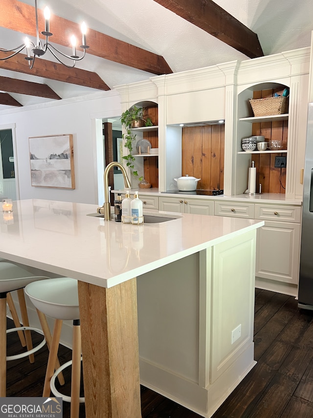 kitchen with white cabinetry, dark wood-type flooring, beamed ceiling, a large island with sink, and a breakfast bar