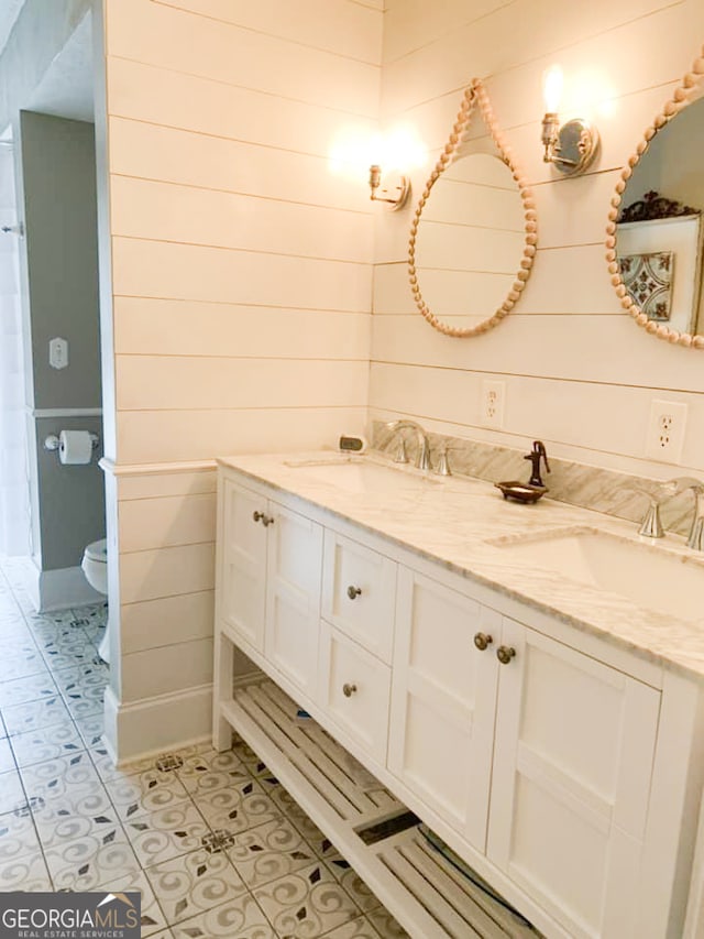 bathroom featuring tile patterned floors, wooden walls, vanity, and toilet