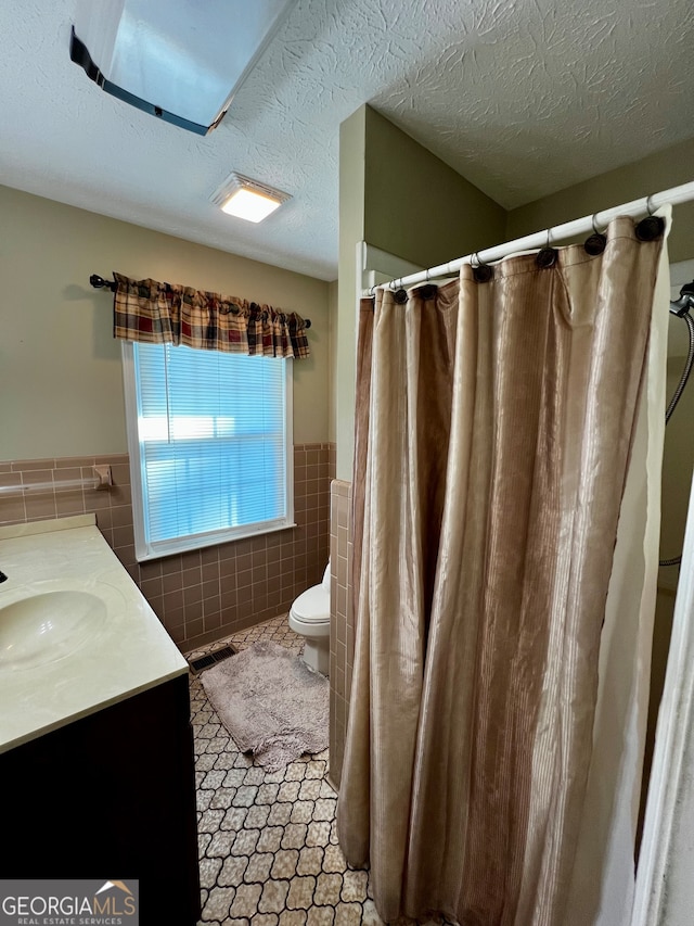 bathroom with vanity, a shower with curtain, toilet, a textured ceiling, and tile walls