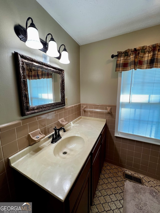 bathroom with a textured ceiling, vanity, a healthy amount of sunlight, and tile walls