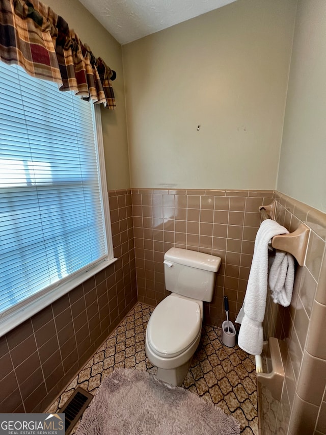 bathroom featuring tile patterned floors, toilet, tile walls, and a textured ceiling