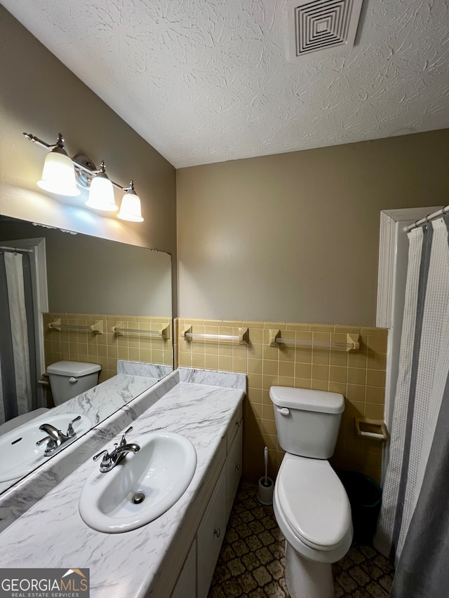 bathroom with vanity, a textured ceiling, toilet, and tile walls