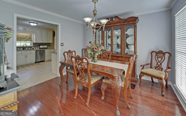 dining room featuring ornamental molding, sink, a chandelier, and light hardwood / wood-style flooring