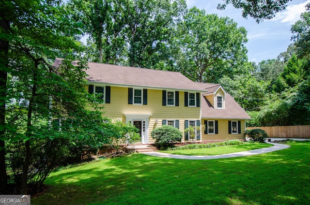 colonial house featuring a front lawn, fence, and a shingled roof