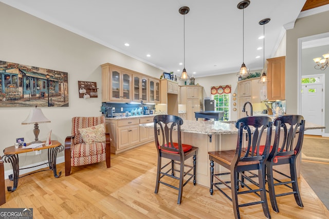 kitchen with ornamental molding, light stone counters, a kitchen breakfast bar, and light hardwood / wood-style flooring