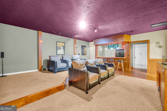 carpeted home theater featuring a textured ceiling, wood walls, and rail lighting