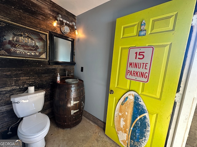 bathroom featuring wood walls, toilet, and concrete flooring