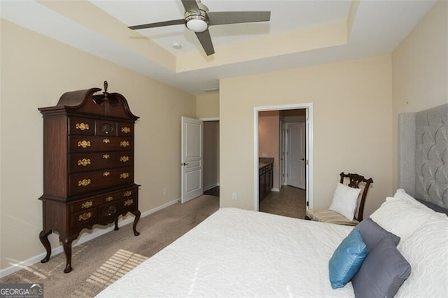 bedroom with a raised ceiling, light colored carpet, connected bathroom, and ceiling fan