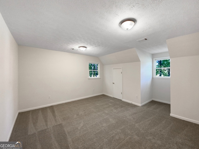 bonus room with lofted ceiling, dark carpet, and a textured ceiling