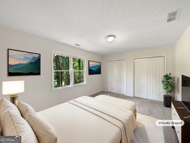 bedroom featuring light carpet, multiple closets, and a textured ceiling