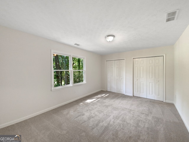 unfurnished bedroom featuring multiple closets, a textured ceiling, and carpet