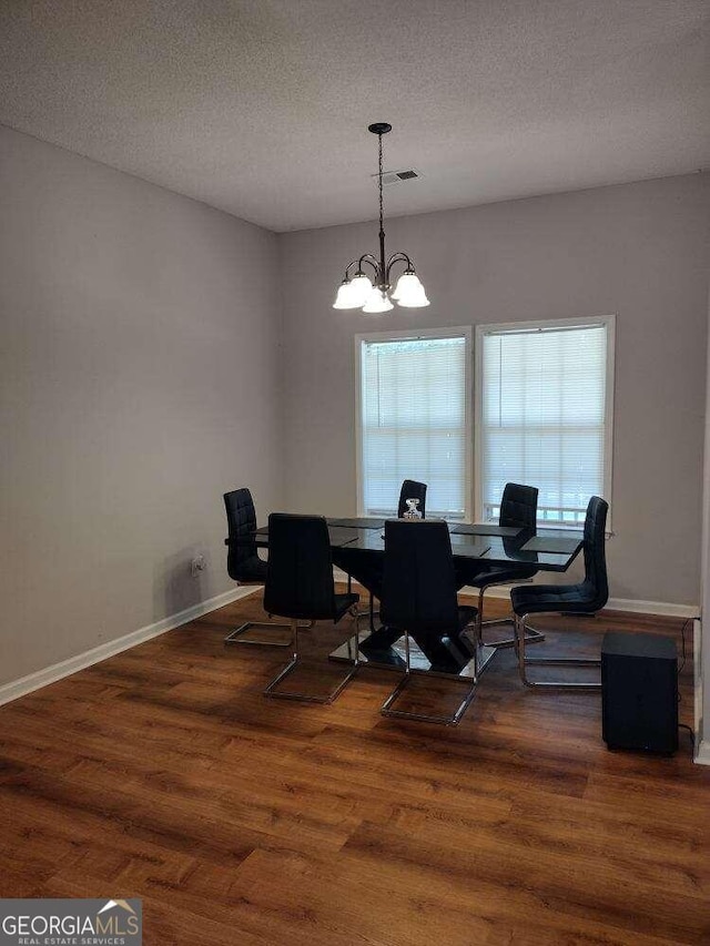 dining room featuring dark wood-type flooring, an inviting chandelier, and a textured ceiling