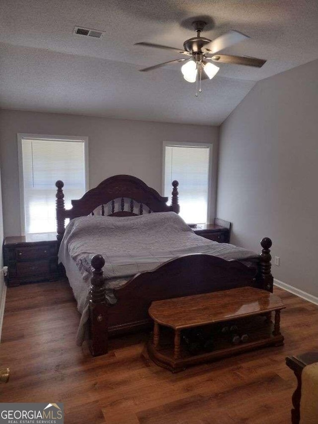 bedroom with ceiling fan, dark wood-type flooring, vaulted ceiling, and a textured ceiling