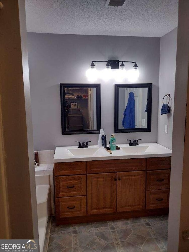 bathroom with a tub, vanity, and a textured ceiling