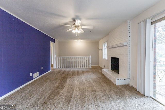 unfurnished living room featuring a textured ceiling, a brick fireplace, carpet floors, and ceiling fan