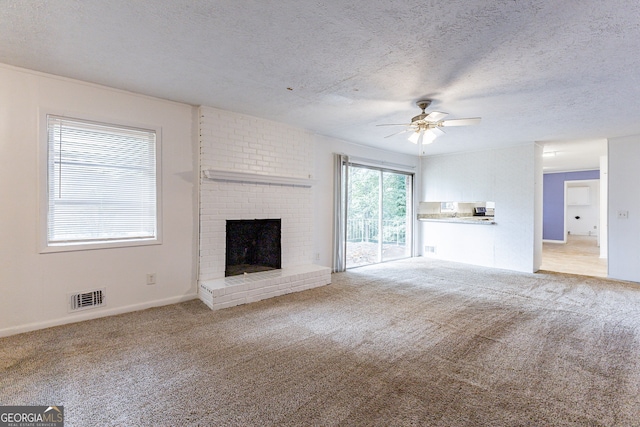 unfurnished living room featuring a textured ceiling, a brick fireplace, light colored carpet, and ceiling fan