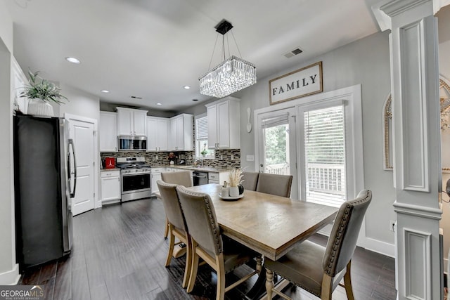 dining space with dark wood-type flooring, a notable chandelier, decorative columns, and sink