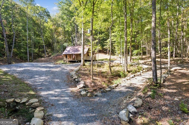 view of front of home with an outbuilding, gravel driveway, and a wooded view