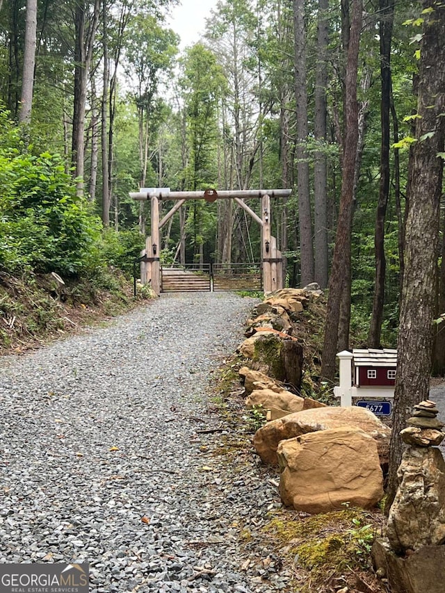 view of street featuring driveway, a forest view, a gate, and a gated entry