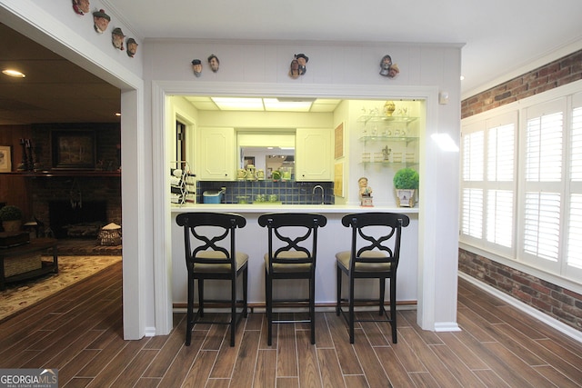 kitchen with a kitchen bar, dark hardwood / wood-style flooring, kitchen peninsula, white cabinetry, and brick wall