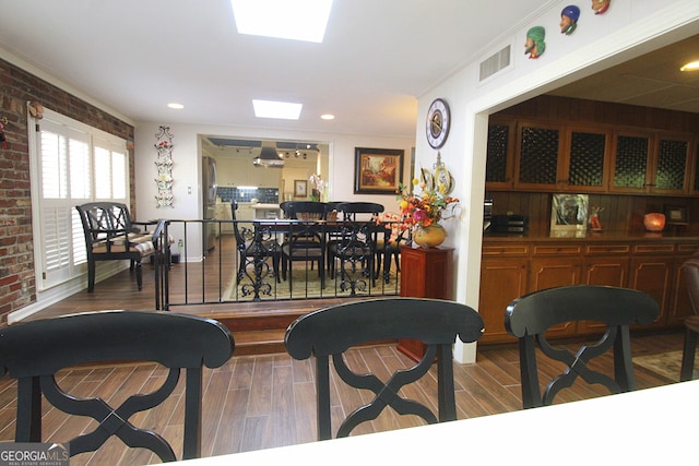 dining room with hardwood / wood-style floors, ornamental molding, and brick wall