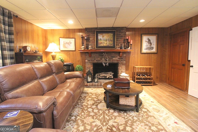 living room with wood walls, light hardwood / wood-style floors, and a brick fireplace