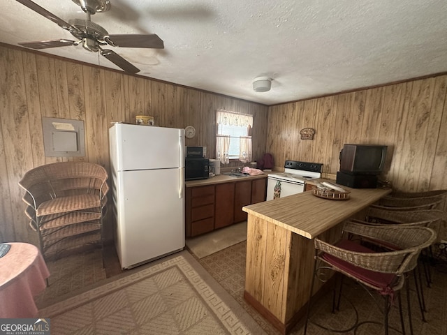 kitchen with light countertops, a peninsula, wood walls, and white appliances