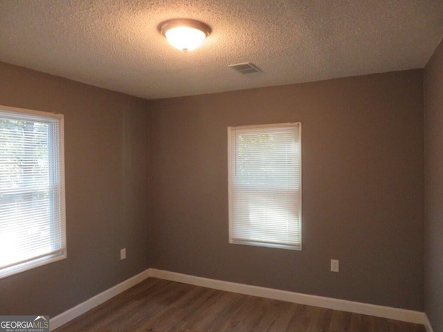 unfurnished room with baseboards, a healthy amount of sunlight, a textured ceiling, and dark wood-style flooring