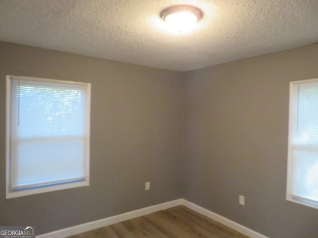 spare room featuring wood finished floors, a textured ceiling, and baseboards