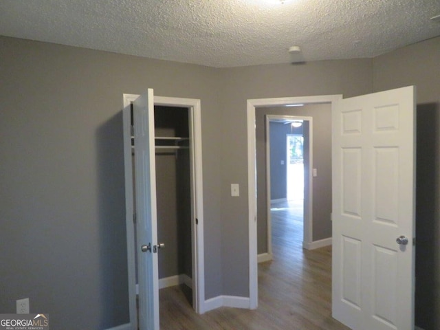 unfurnished bedroom featuring baseboards, wood finished floors, a textured ceiling, and a closet