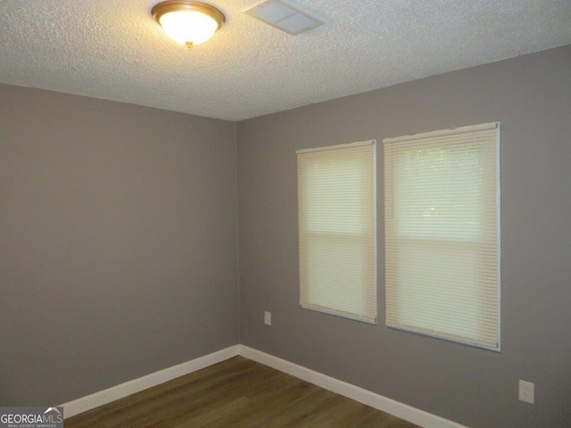 unfurnished room with baseboards, visible vents, dark wood-type flooring, and a textured ceiling
