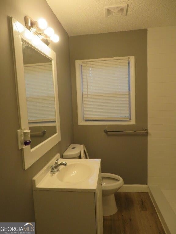 bathroom featuring wood finished floors, visible vents, toilet, vanity, and a shower
