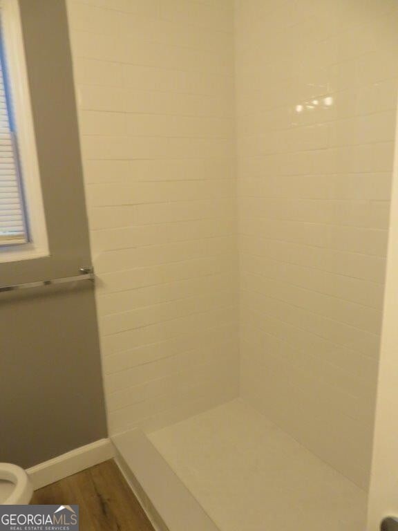 bathroom featuring tiled shower, toilet, and wood-type flooring