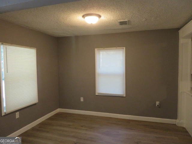 unfurnished room with baseboards, visible vents, wood finished floors, and a textured ceiling