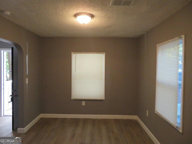 unfurnished room with arched walkways, wood finished floors, a textured ceiling, and visible vents