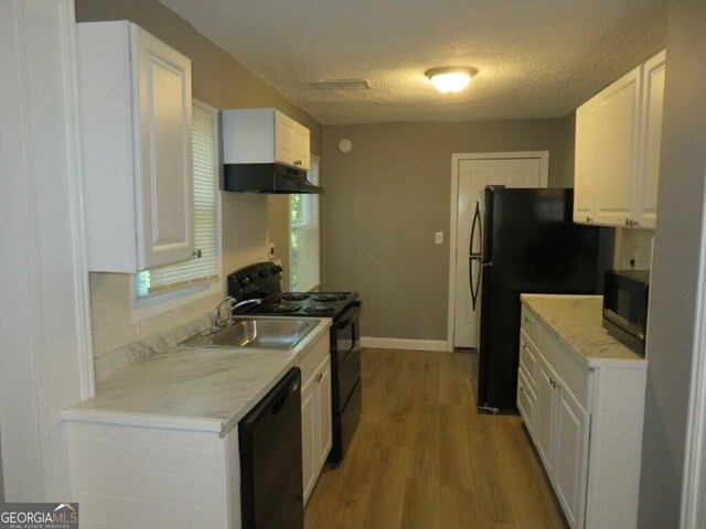 kitchen featuring a sink, a textured ceiling, light wood-type flooring, under cabinet range hood, and black appliances