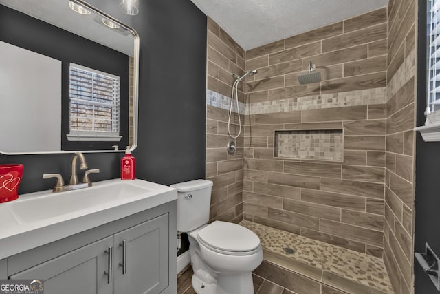 bathroom featuring vanity, toilet, tiled shower, and a textured ceiling