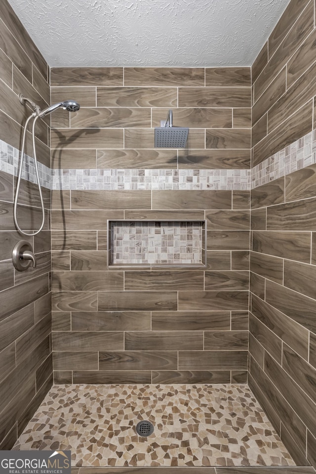 bathroom with a tile shower and a textured ceiling