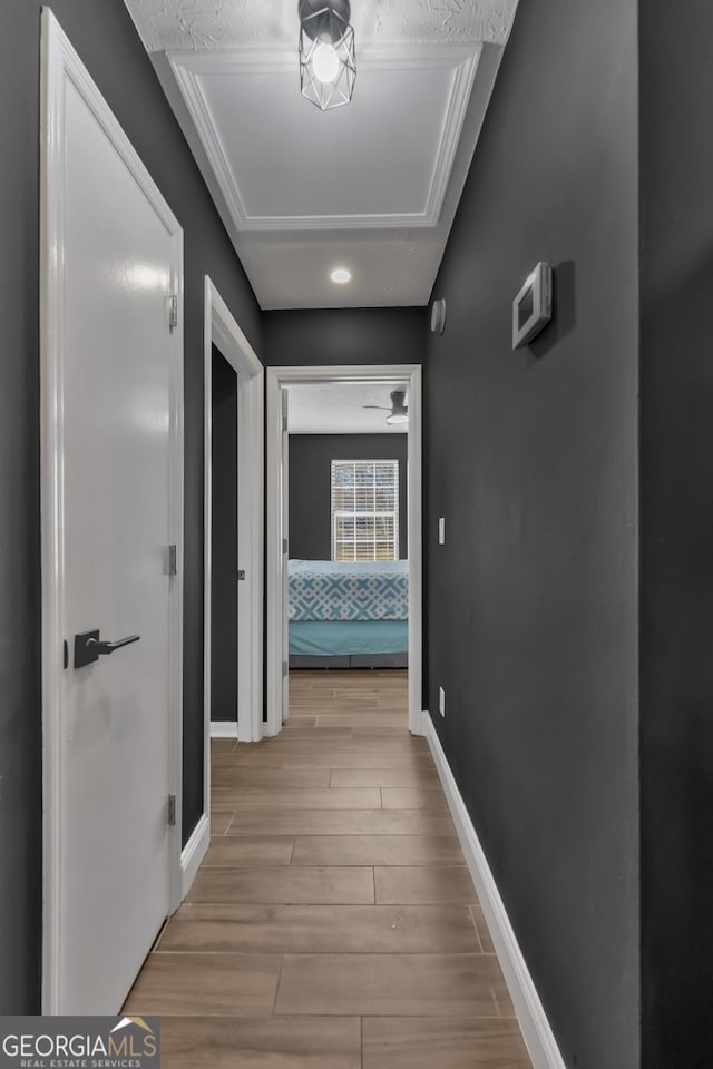 hall with light hardwood / wood-style floors, ornamental molding, and a textured ceiling