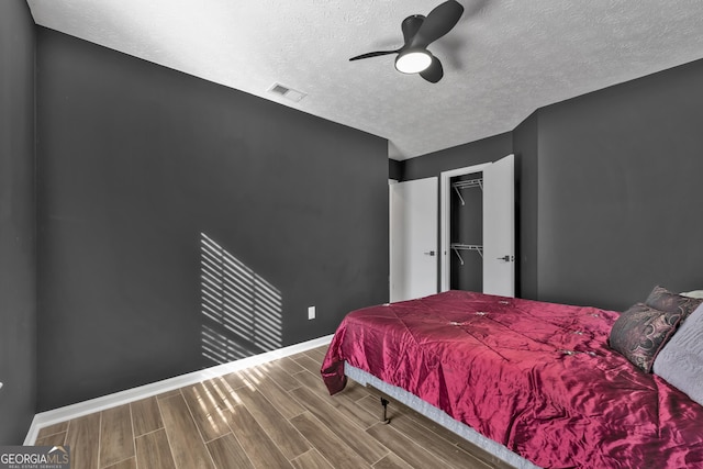 bedroom with a walk in closet, hardwood / wood-style flooring, ceiling fan, a textured ceiling, and a closet