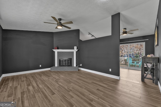 unfurnished living room featuring hardwood / wood-style flooring, a fireplace, ceiling fan, and a textured ceiling