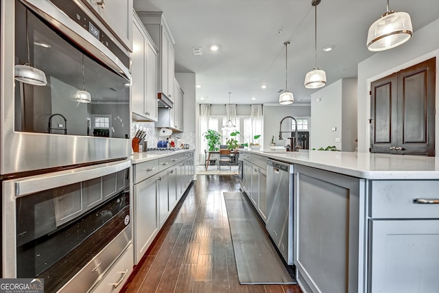 kitchen with a large island with sink, decorative light fixtures, appliances with stainless steel finishes, and dark hardwood / wood-style flooring