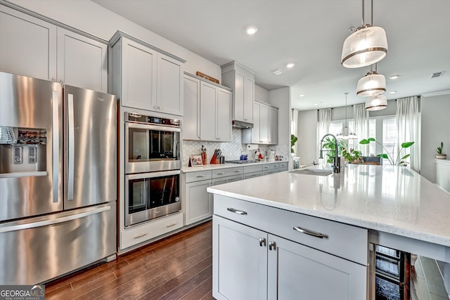 kitchen featuring light stone counters, stainless steel appliances, hanging light fixtures, and sink