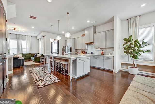 kitchen with dark wood-type flooring, hanging light fixtures, a center island with sink, and a kitchen breakfast bar